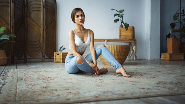 Игривая девушка в джинсах и лифчике демонстрирует соблазнительные позы на полу