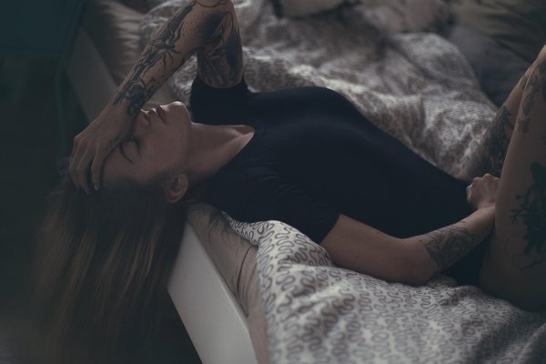 Жгучая девушка с татуировками лежит на спине